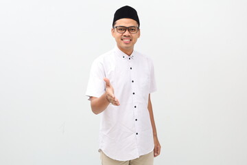 Asian muslim man over isolated white background smiling friendly offering handshake as greeting and...