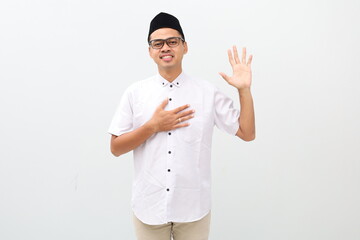 Muslim Asian man looking to the camera with happy face expression while waving his hand to greet...
