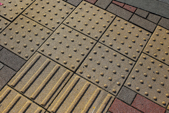 Yellow tactile paving guiding path for visually impaired people on a city sidewalk and street crossing.