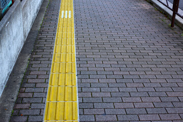 Yellow tactile paving guiding path for visually impaired people on a city sidewalk and street...