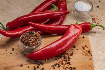 The pods of red chilli pepper, glass cup of peppercorn,  bowl of salt on wooden cutting board....