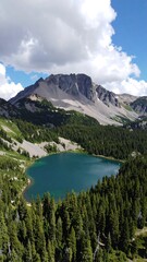 Obraz premium A serene alpine lake nestled within a verdant coniferous forest, overlooked by a majestic mountain under a partly cloudy sky