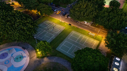 Aerial View of Illuminated tennis courts at Dusk Surrounded by Lush Green Trees