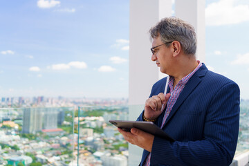 Caucasian businessman writing on tablet with stylus, standing on skyscraper, concept of real estate...