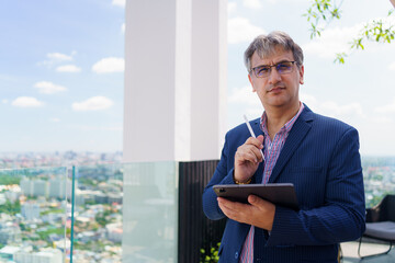 Caucasian businessman writing on tablet with stylus, standing on skyscraper, concept of real estate...