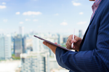 Caucasian businessman writing on tablet with stylus, standing on skyscraper, concept of real estate...