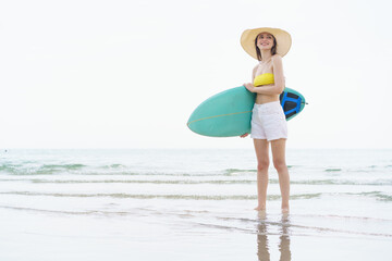 Smiling woman poses with surfboard on a bright beach day.