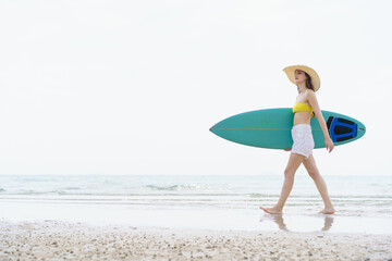 Smiling woman poses with surfboard on a bright beach day.