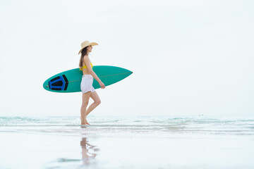 Smiling woman poses with surfboard on a bright beach day.
