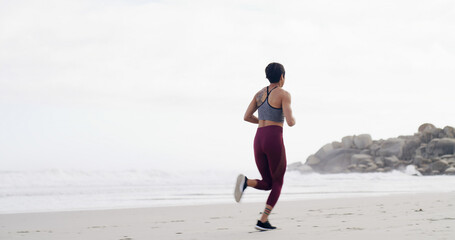 Woman, running and back at beach, training and fitness with space, sky and outdoor with routine. Person, workout and exercise for wellness, cardio challenge and jog by ocean for health in New Zealand