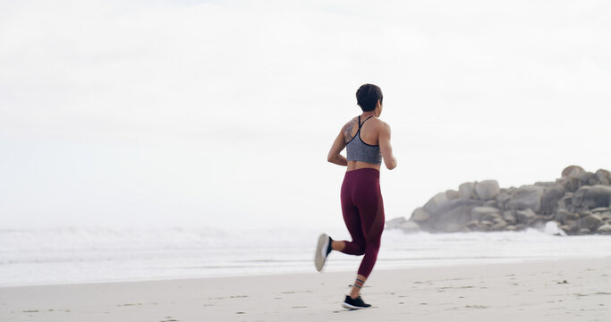 Woman, running and back at beach, training and fitness with space, sky and outdoor with routine. Person, workout and exercise for wellness, cardio challenge and jog by ocean for health in New Zealand
