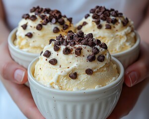 Three small bowls of vanilla ice cream topped with chocolate chips, held in hands