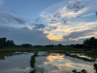 Peaceful countryside sunset with dramatic cloudy sky reflecting on calm water in rural landscape,...