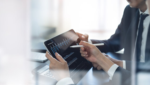 Businessman having a discussion with colleague, working together in office. Two asian business people using digital tablet at meeting. teamwork and collaboration - Powered by Adobe