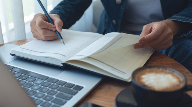 Businesswoman planning agenda and schedule, writing on calendar event planner notebook. Woman hand writing on plan reminder for work project and monthly event schedule on office table, close up