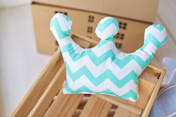 Chevron pattern pillow in shape of crown on wooden crate near cardboard box.