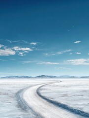 Fototapeta premium a winding tire track cuts through an endless expanse of snow or salt flats under a vast blue sky with distant mountains on the horizon creating a serene yet mysterious atmosphere