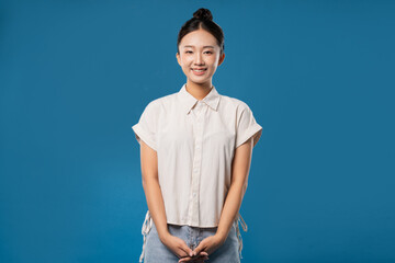 Smiling Asian woman in collared shirt with arms folded looking at camera against blue background