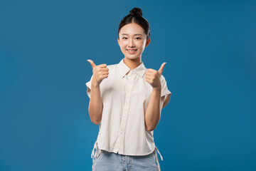 Smiling woman with hair in a bun wearing a white button-down shirt and jeans giving thumbs up