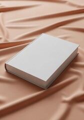 Fototapeta premium A white book resting on a peach colored satin fabric background view