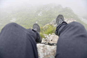 Hiker's Perspective: Resting on a Rocky Cliff Edge in Foggy Weather