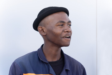 single african worker, in workwear uniform with a beanie standing in front of a warehouse wall