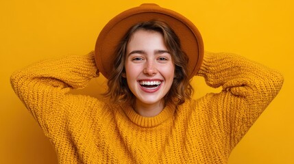 happy playful young woman smiles broadly shows white teeth keeps hands on hat dressed in casual jumper expresses sincere emotions being in good mood isolated over yellow background joy concept no log