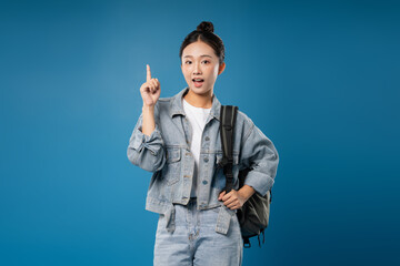 Enthusiastic student pointing upwards with a backpack on a solid blue background Got the idea!