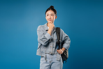 Thoughtful Student: A young woman in a denim outfit contemplates a question against a blue backdrop