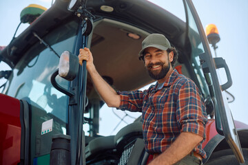 Happy farmer getting into his tractor while working in agricultural field and looking at camera. © Drazen