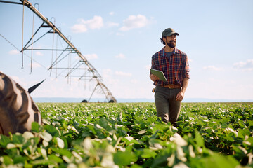 Happy farmer with digital tablet walking through the crops.