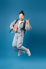 Obraz premium Energetic student leaps holding a book in a joyful pose against a vibrant blue backdrop