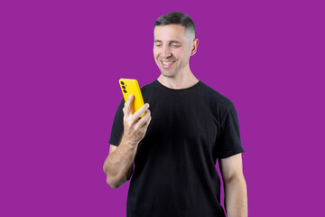 A man is smiling while holding a yellow phone. Purple isolated background