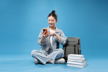 Asian student studying and texting on smartphone sitting on the floor with books and backpack