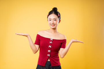 Smiling woman in red top presents space with hands against a yellow background Studio shot