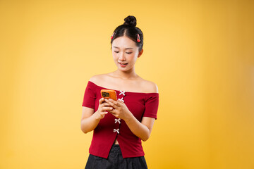 Smiling woman in red top using a mobile phone in a studio setting against a yellow background