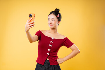 Smiling woman taking a selfie with a cellphone in front of a yellow background in a studio setting