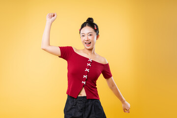 Cheerful woman with raised fist in celebratory pose against warm yellow backdrop radiating joy