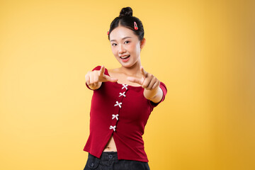Cheerful young woman pointing at the viewer with a confident and playful expression on a yellow...