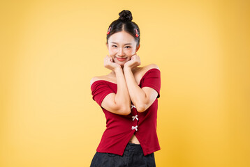 A smiling young woman with hands on her cheeks wearing a stylish off-the-shoulder top on yellow