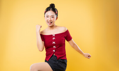 Young woman strikes a celebratory pose on a yellow background displaying an expression of joy