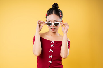 Stylish Asian woman with sunglasses red top and hair clips poses against a yellow background