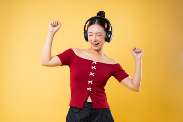 Young woman dances with headphones eyes closed against a yellow backdrop enjoying music