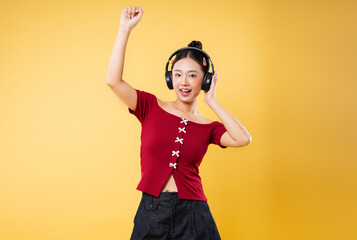 Young woman with headphones dancing against a yellow background She is happy and energetic