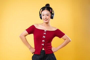 A young woman poses in a red top and headphones smiling against a vibrant yellow backdrop