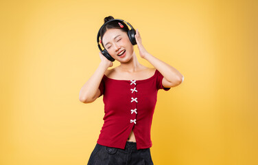 Young woman with headphones listening to music eyes closed feeling the rhythm yellow background