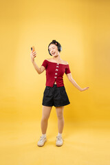 Woman enjoys music with headphones dances with phone against vibrant yellow backdrop in studio