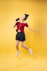 Enthusiastic Woman Jumps in Joy While Holding Her Mobile and Listens to Music With Headphones