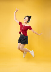 Joyful young woman jumps with headphones on against a yellow backdrop She's smiling and carefree