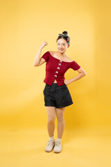 Smiling woman in red top flexing arm She has sunglasses on her head against a yellow background